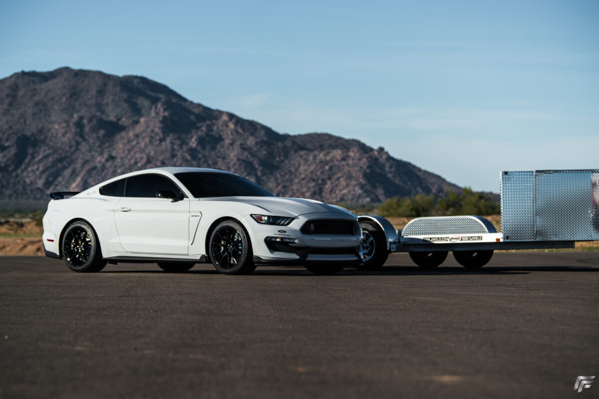 White Ford Mustang Parked Next To A Jimglo Ego Tilt Bed Trailer